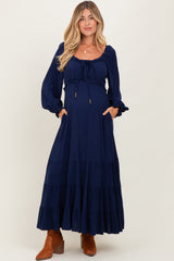 woman wearing a navy blue maternity maxi dress with long sleeves and a drawstring neckline, holding her baby bump
