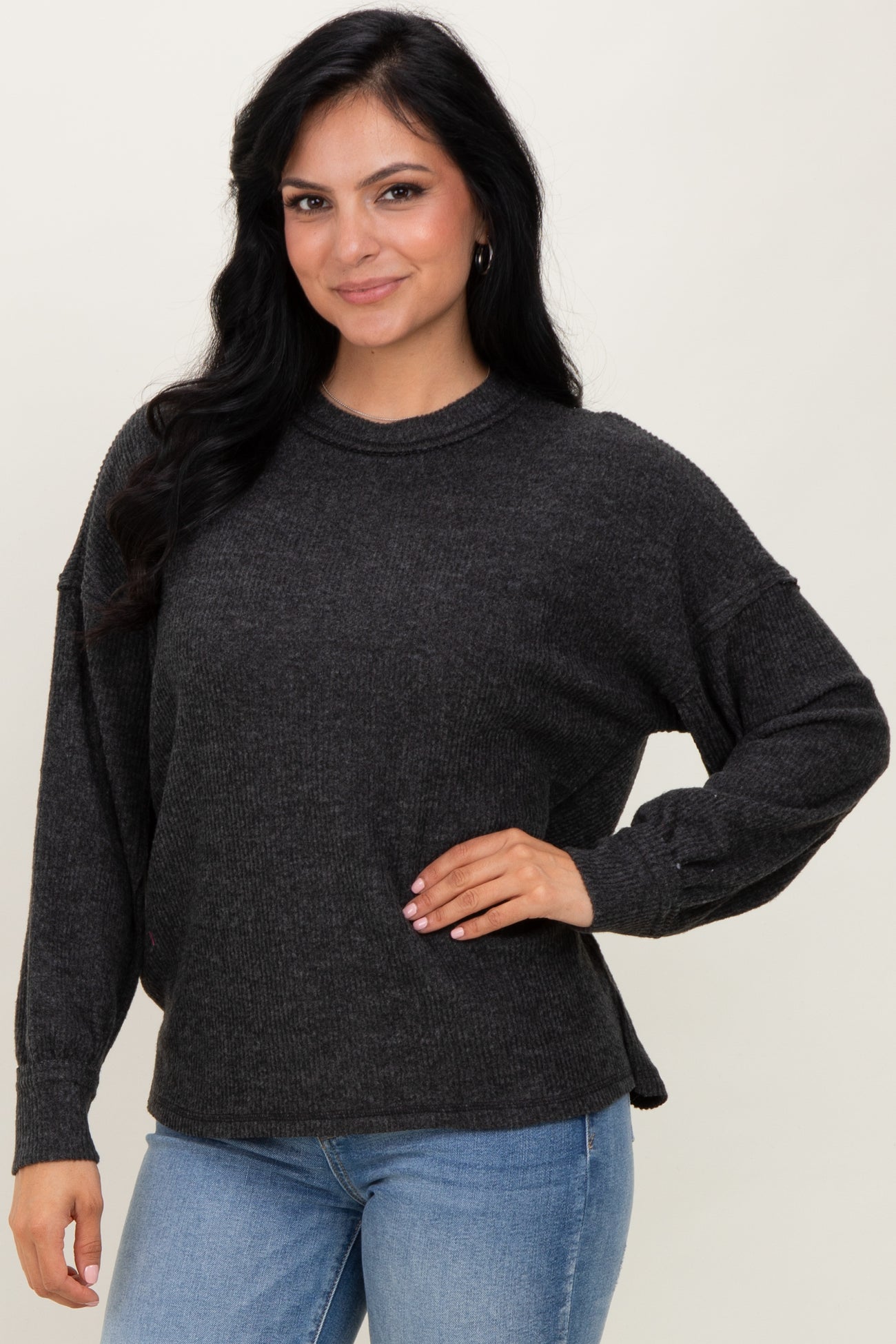 woman wearing a dark gray oversized sweater with long sleeves and side slits, paired with light blue jeans