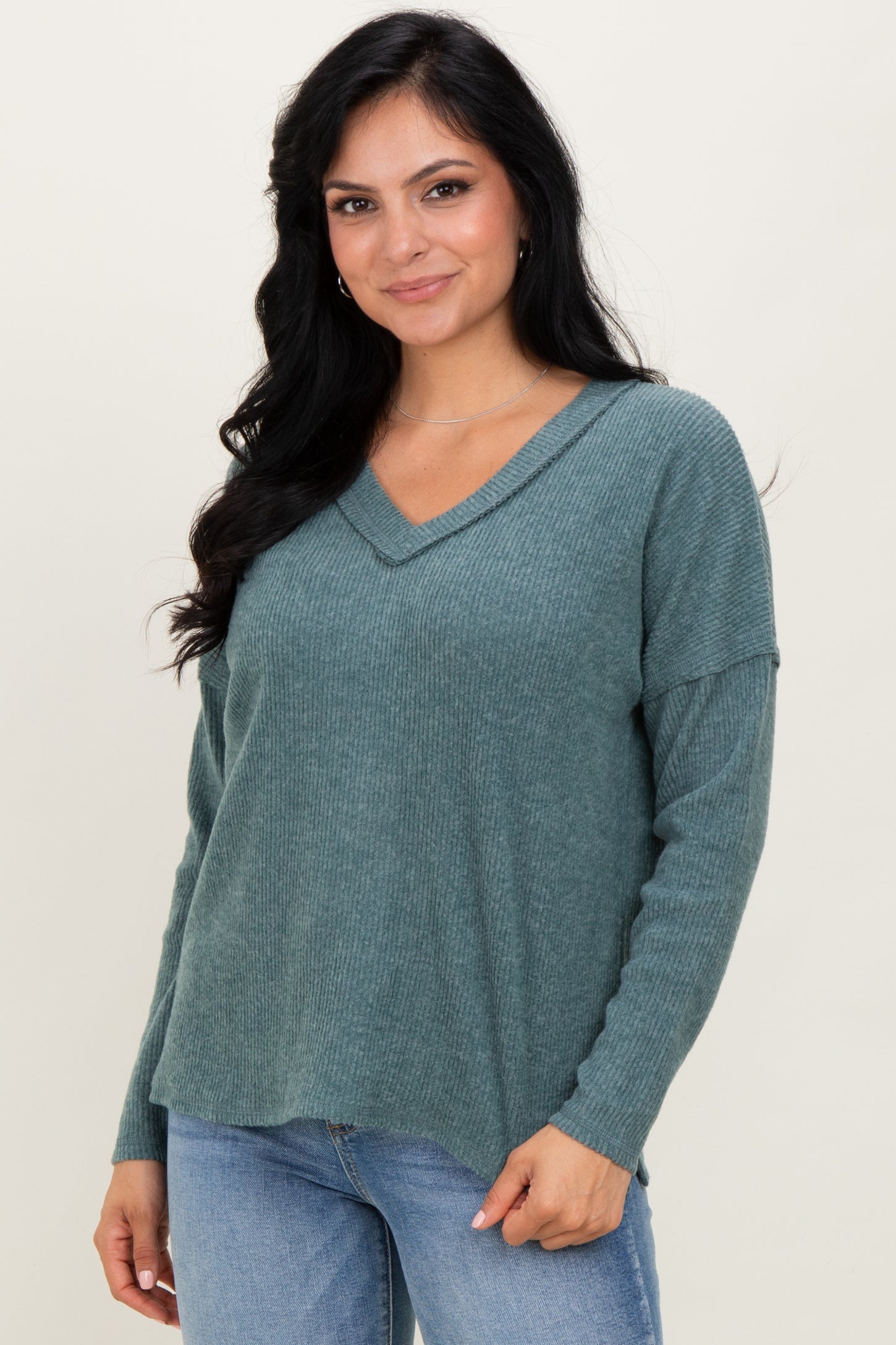 woman wearing a teal v-neck knit sweater with long sleeves and a relaxed fit, paired with light blue jeans