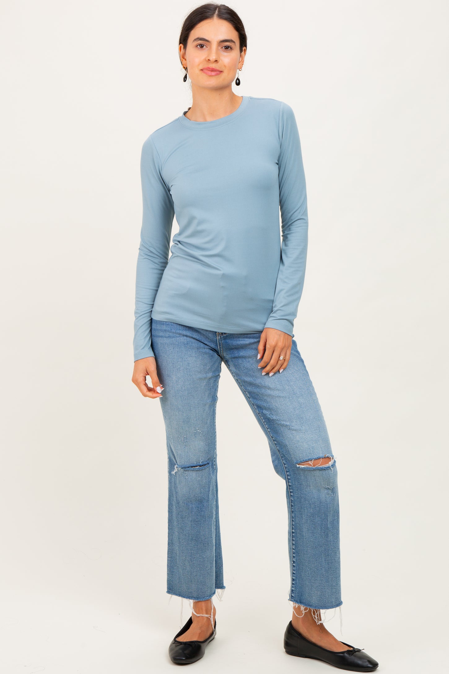 woman wearing a light blue long sleeve top paired with distressed jeans and black flats