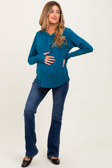 woman wearing a teal maternity top with buttons and flared jeans, showing her baby bump