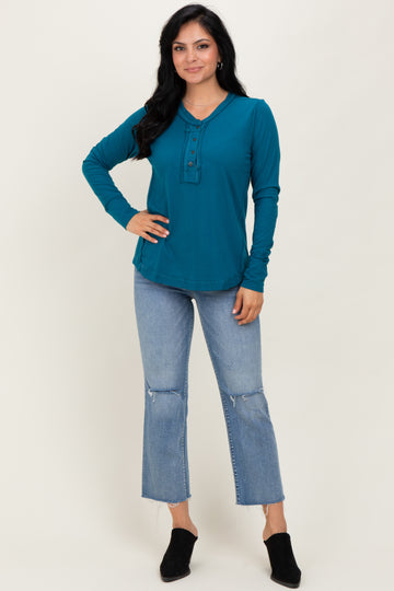 woman wearing a teal long sleeve henley top with buttons, paired with distressed light blue jeans and black mules