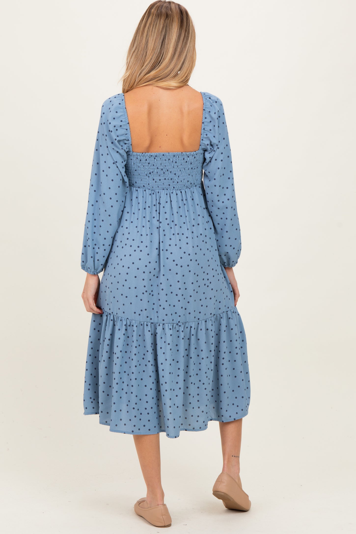 woman wearing a blue polka dot maternity dress with a smocked back and a tiered skirt