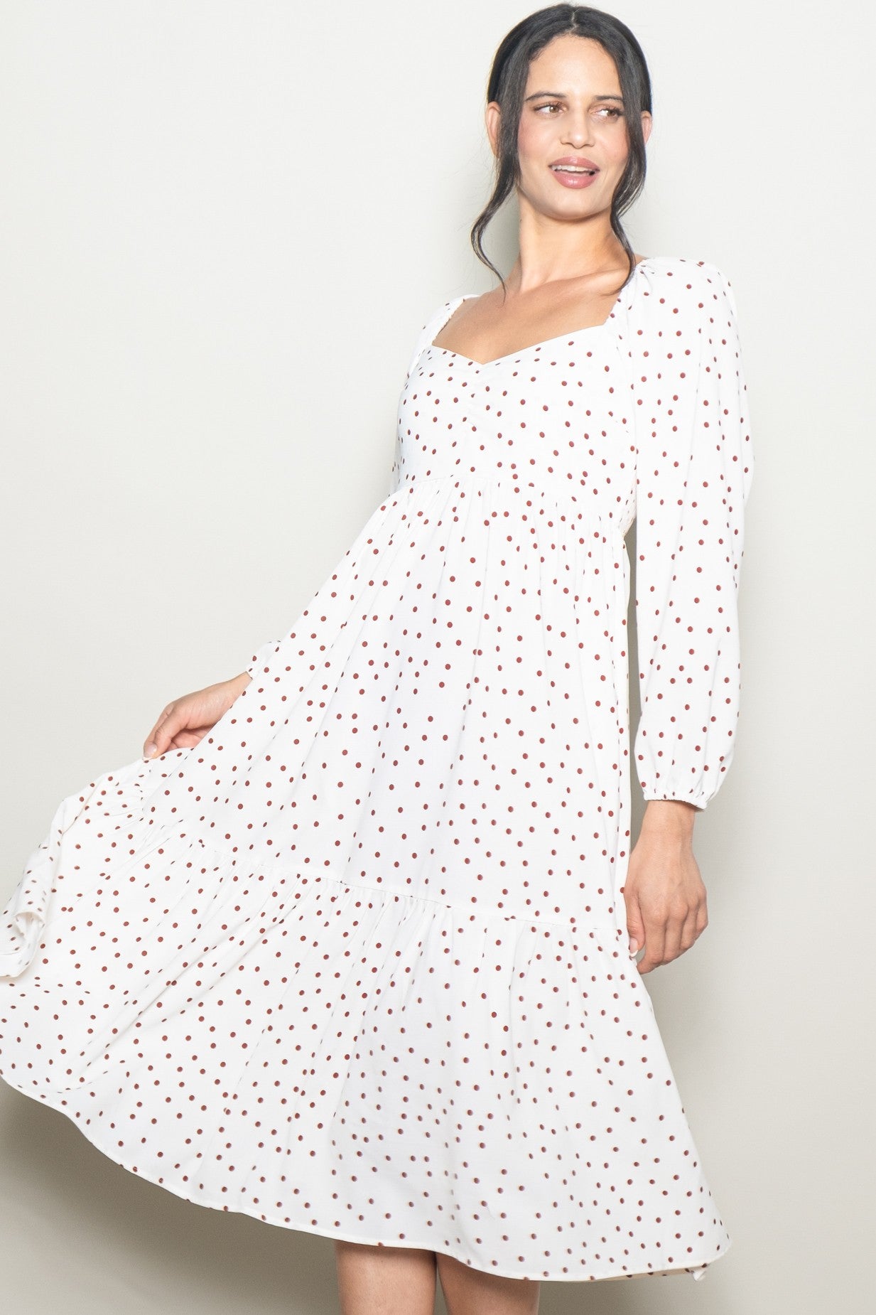 woman wearing a white midi dress with red polka dots and long puff sleeves, spinning slightly towards the camera