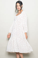 woman wearing a white midi dress with red polka dots and puff sleeves, smiling at the camera