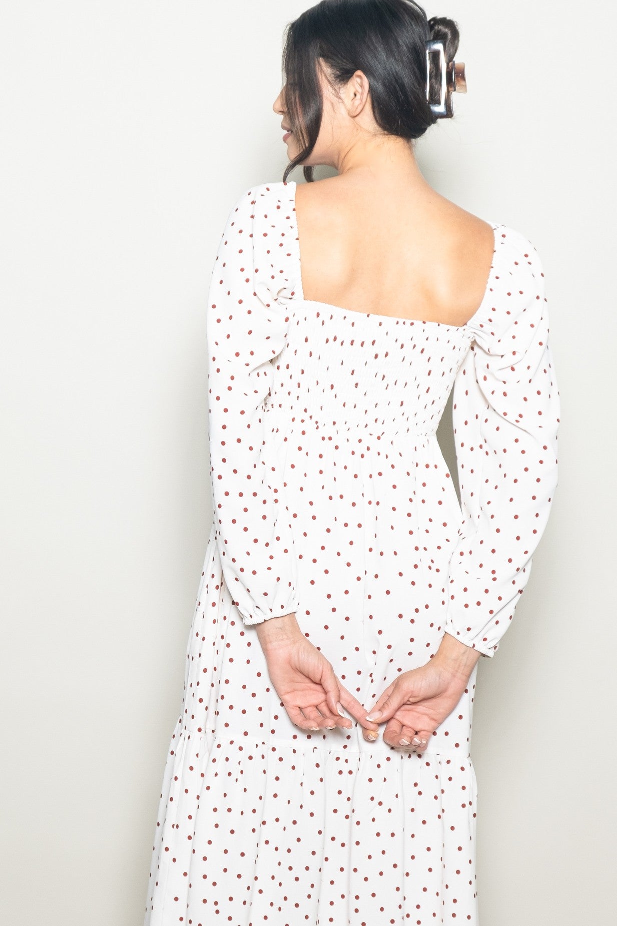 woman wearing a white long sleeve dress with red polka dots and a smocked bodice, seen from the back