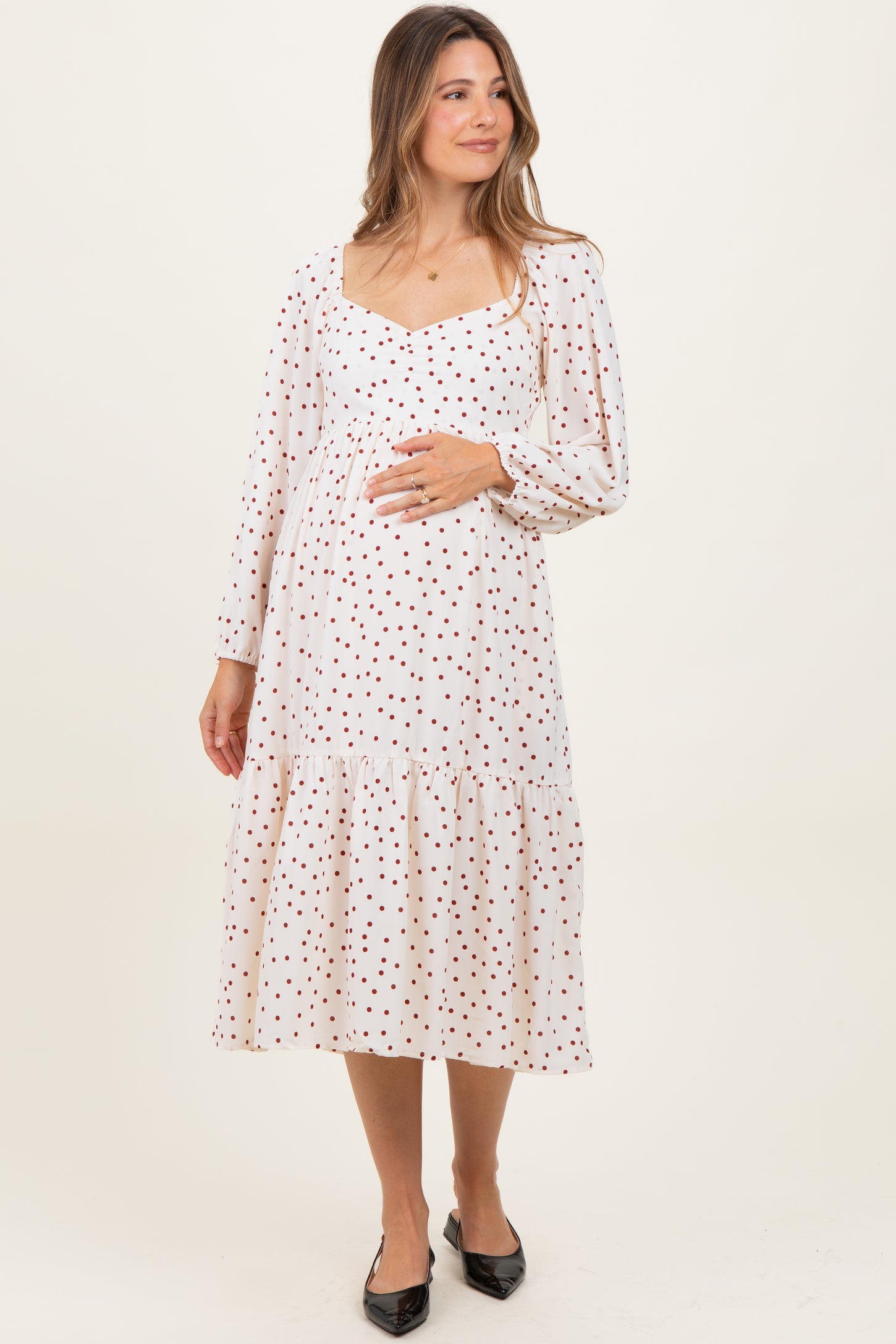 woman wearing a cream maternity dress with red polka dots and a tiered skirt, holding her baby bump