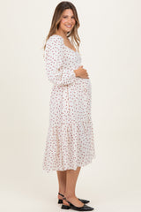 woman wearing a white maternity dress with red polka dots and a tiered skirt, holding her baby bump