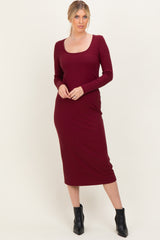 woman wearing a burgundy long sleeve fitted midi dress with a scoop neckline and form-fitting silhouette