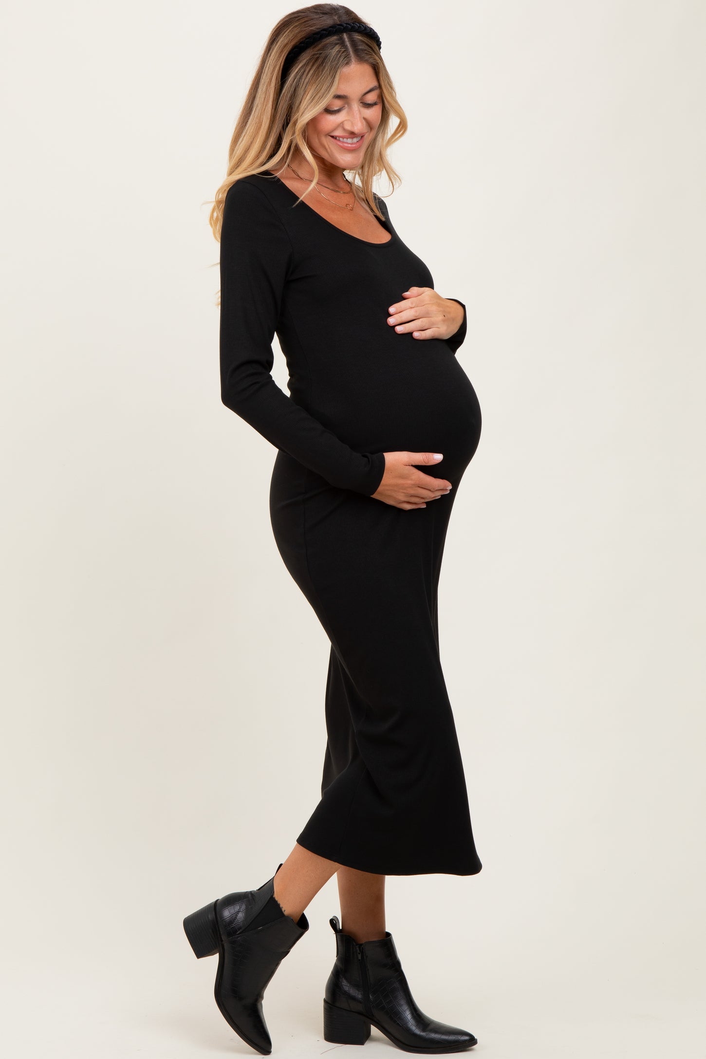 woman wearing a black long sleeve maternity dress, cradling her baby bump, paired with black ankle boots