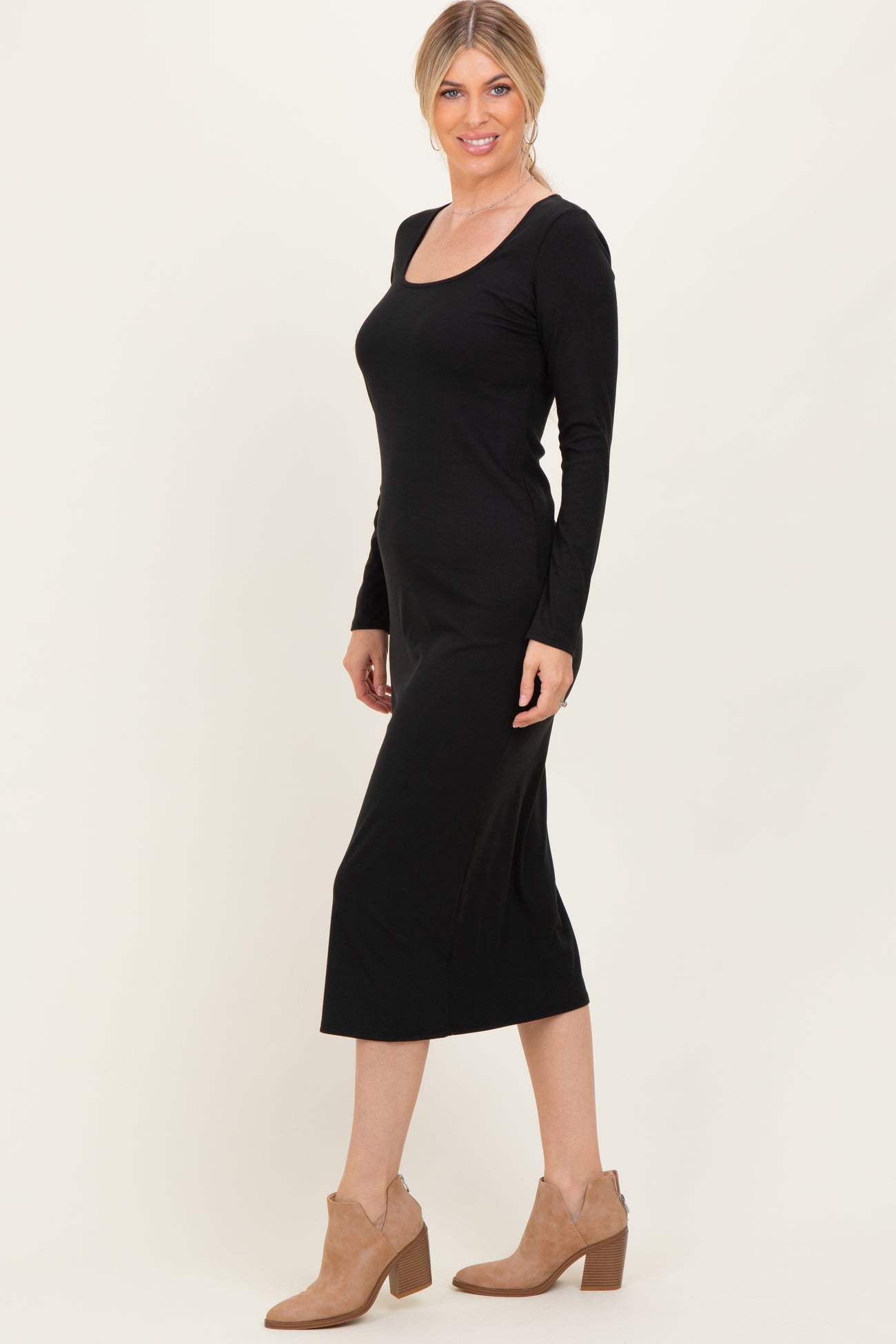 woman wearing a black long sleeve midi dress with a square neckline and styled with tan ankle boots