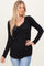 woman wearing a black ribbed long sleeve top with a v-neckline and subtle ruching detail, paired with light blue jeans