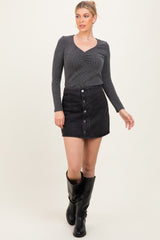 woman wearing a black ribbed long sleeve top and a black button-front mini skirt, paired with knee-high black boots