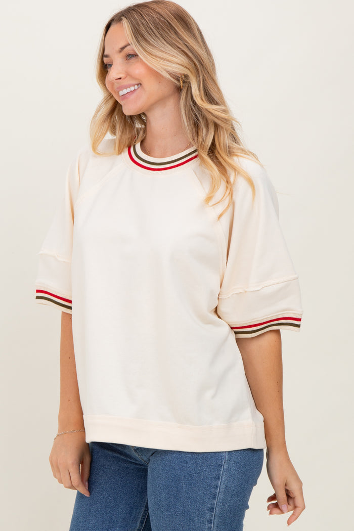 woman wearing a cream short sleeve sweatshirt with red and green striped neckline and sleeve details