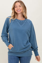 woman wearing a blue oversized sweatshirt with a round neckline and ribbed cuffs, smiling against a neutral background