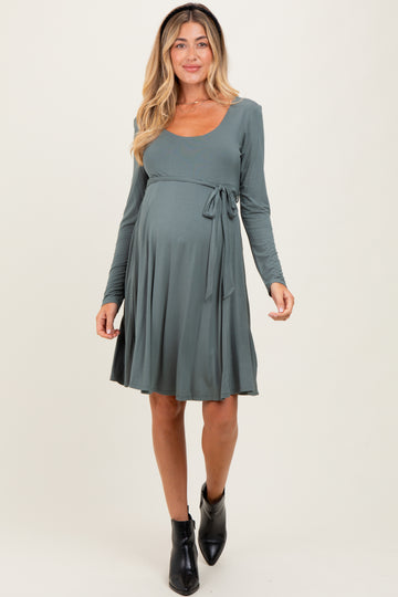 woman wearing a teal long sleeve maternity dress with a tie waist and a visible baby bump