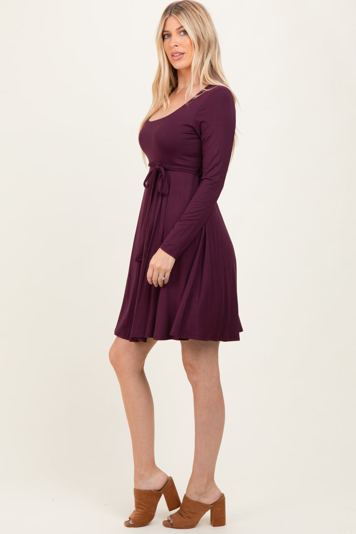 woman wearing a long sleeve plum colored dress with a tie waist and flared skirt