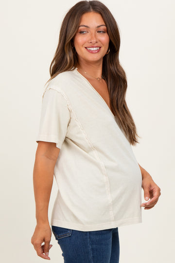 woman wearing a cream-colored maternity top with a v-neck and side ruffle detail, showing her baby bump