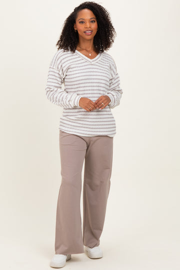 woman wearing a striped v-neck sweater in cream and gray with loose-fitting beige pants and white sneakers