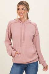 woman wearing a pink ribbed hooded sweatshirt with a front pocket and relaxed fit paired with blue jeans