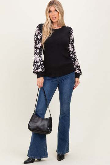 woman wearing a black ribbed sweater with floral patterned sleeves, paired with flared jeans and holding a black handbag