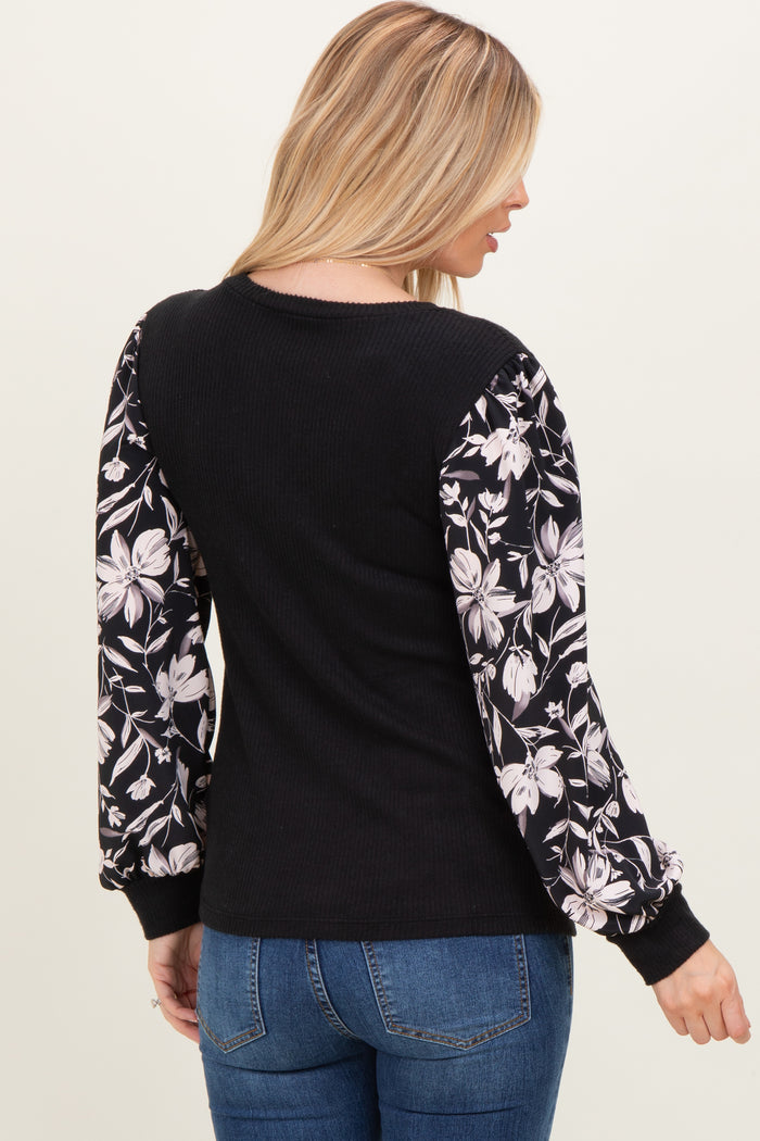 woman wearing a black sweater with floral puff sleeves and blue jeans, shown from the back