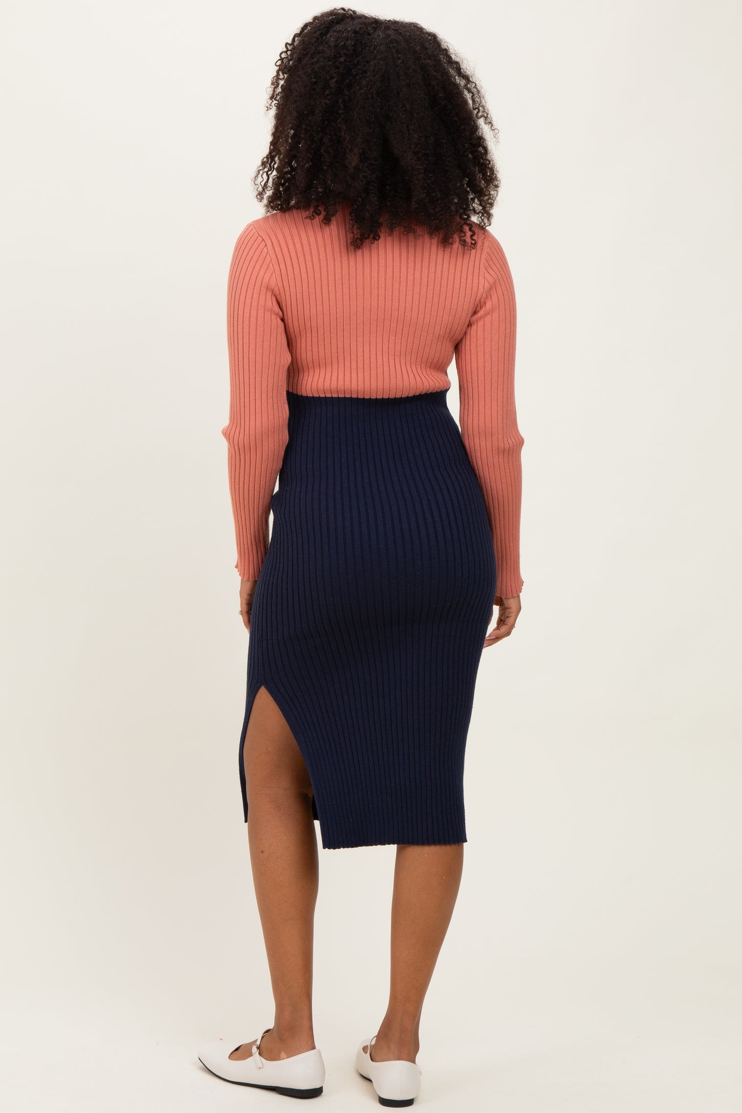 woman wearing a rust-colored ribbed long sleeve top and a navy ribbed midi skirt with a side slit