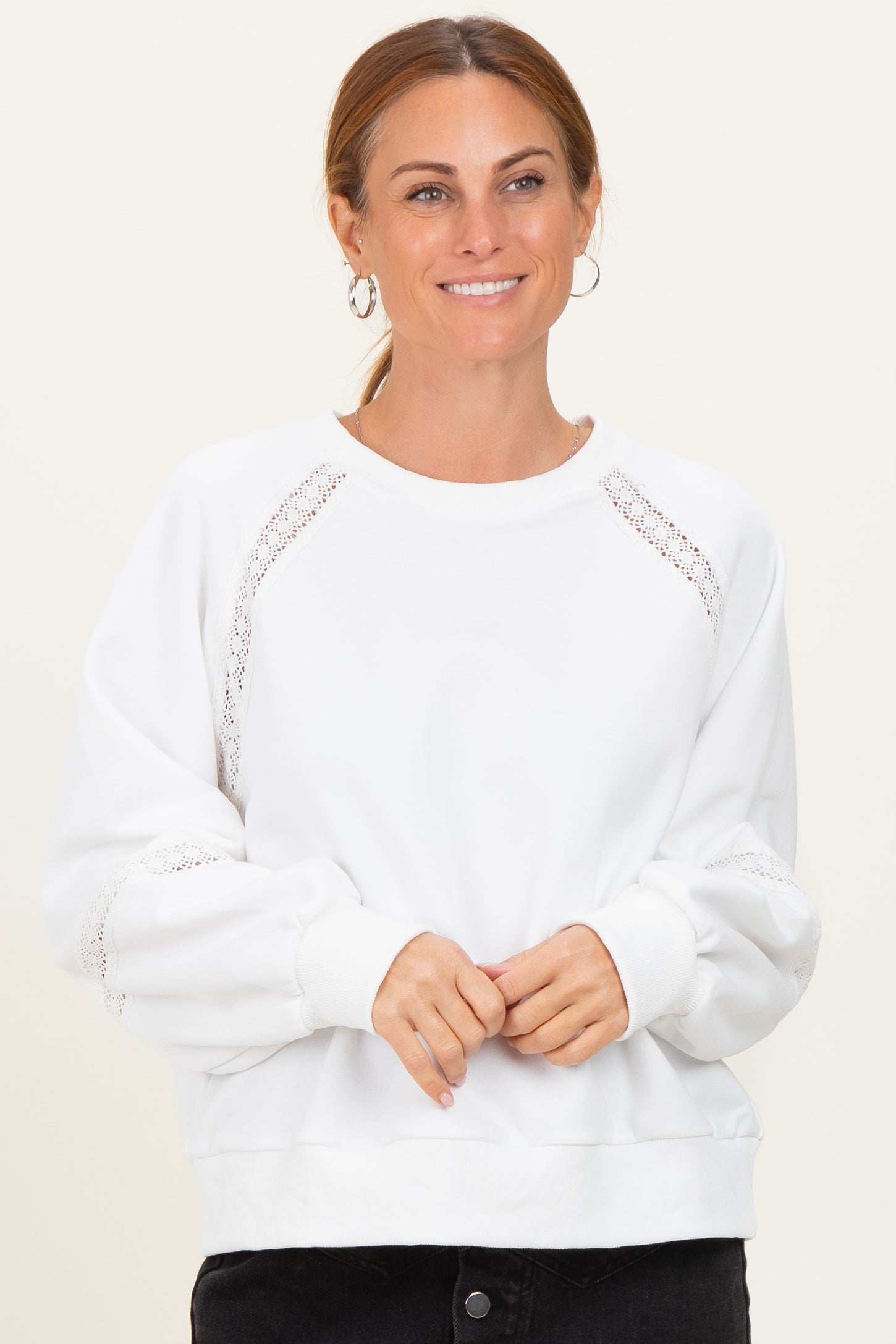 woman wearing a white sweatshirt with lace detail and puff sleeves, smiling against a neutral background