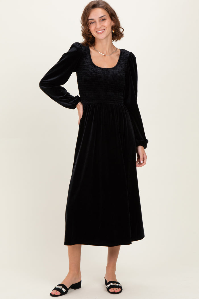 woman wearing a black velvet long sleeve midi dress with a square neckline and smocked bodice, smiling