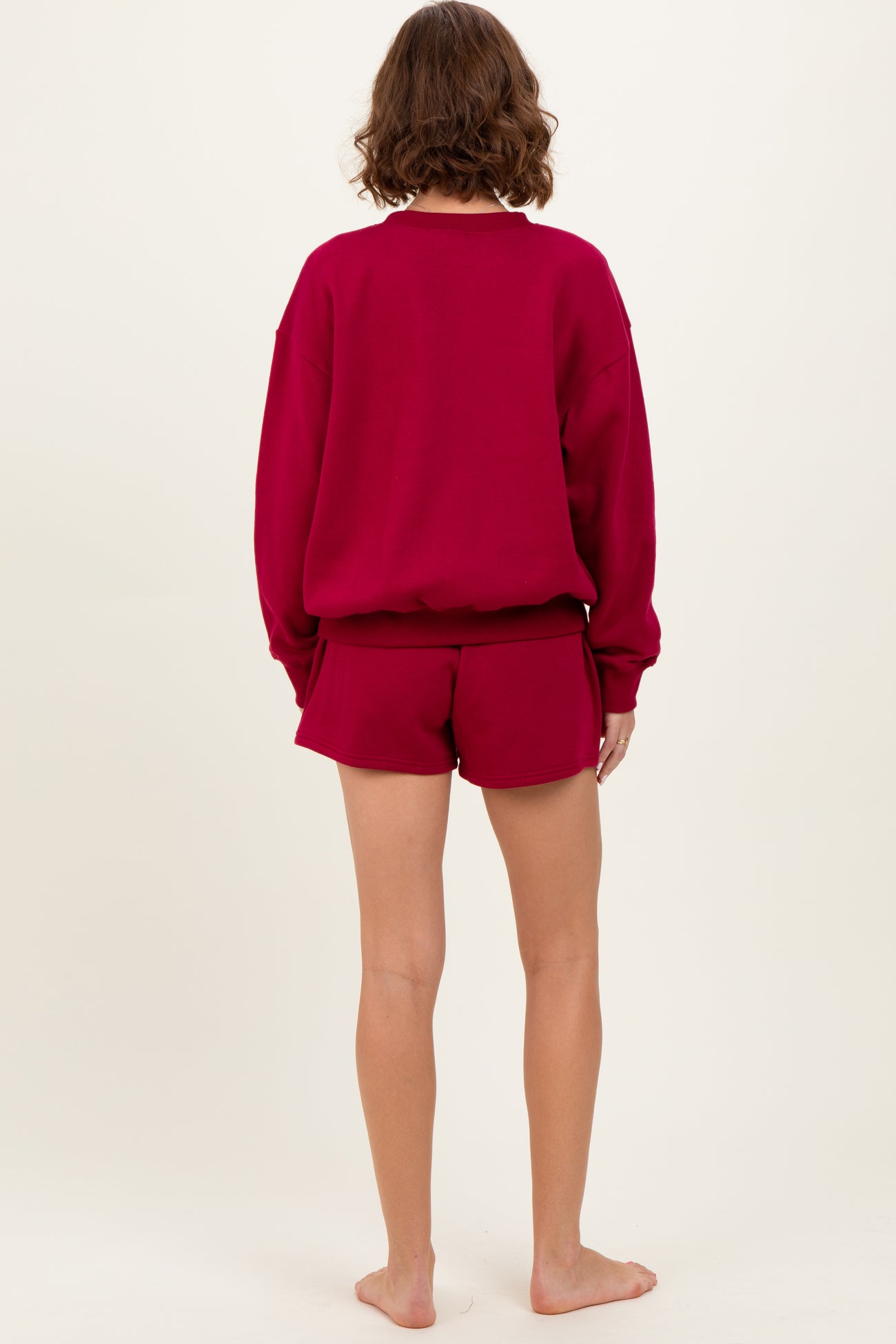 woman wearing a burgundy oversized sweatshirt and matching shorts, viewed from the back