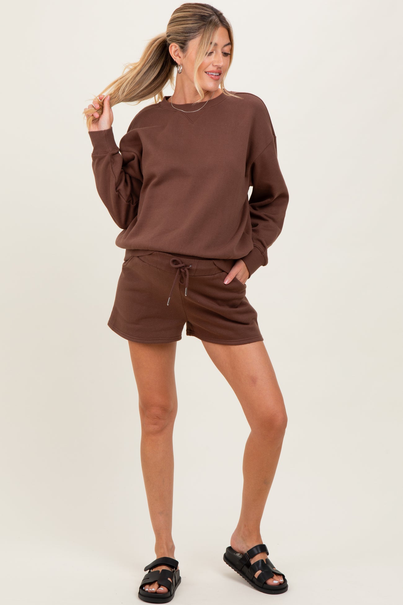 woman wearing a chocolate brown long sleeve maternity sweatshirt and matching shorts, styled casually with sandals
