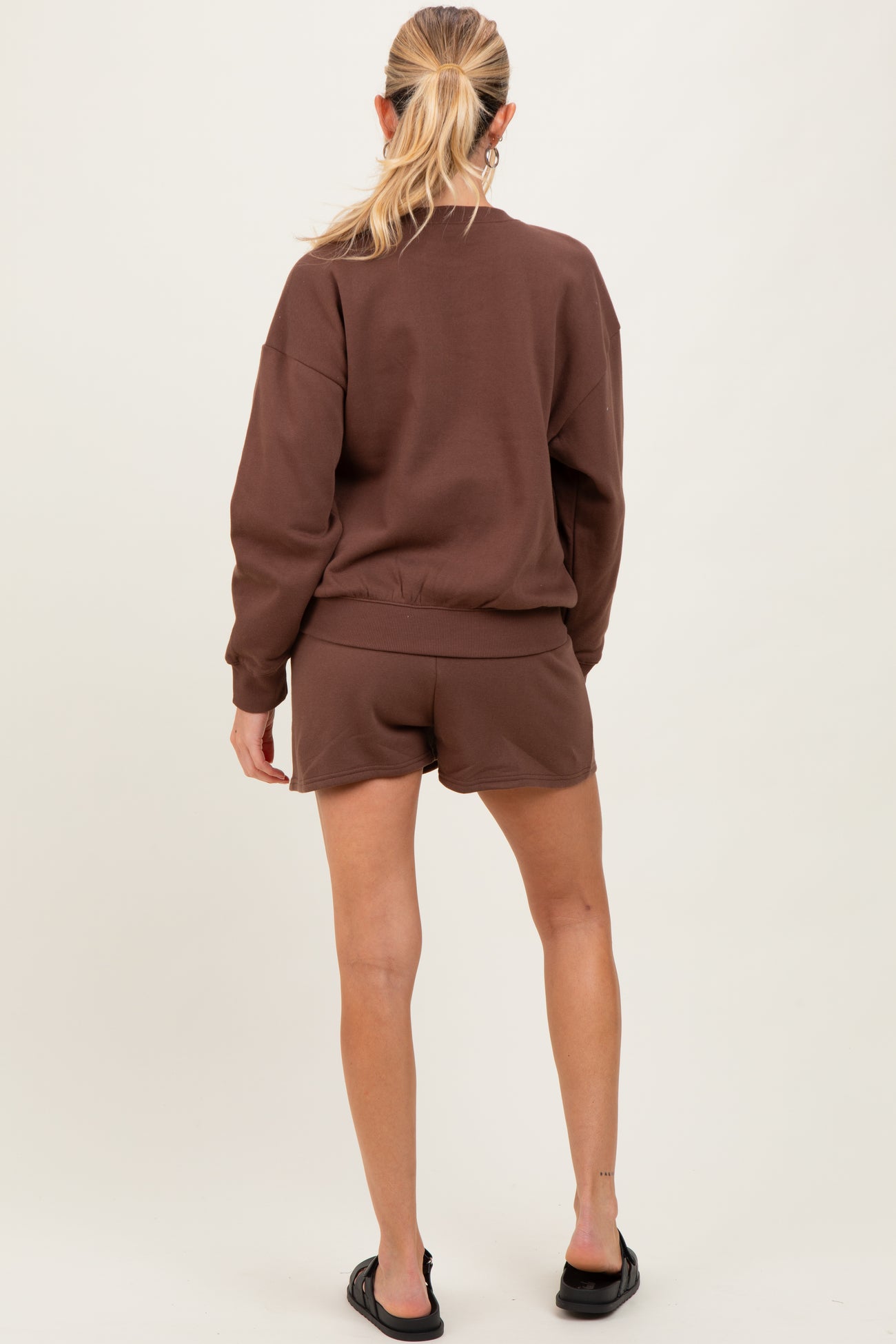 woman wearing a brown maternity sweatshirt and matching shorts, showing a relaxed fit from the back