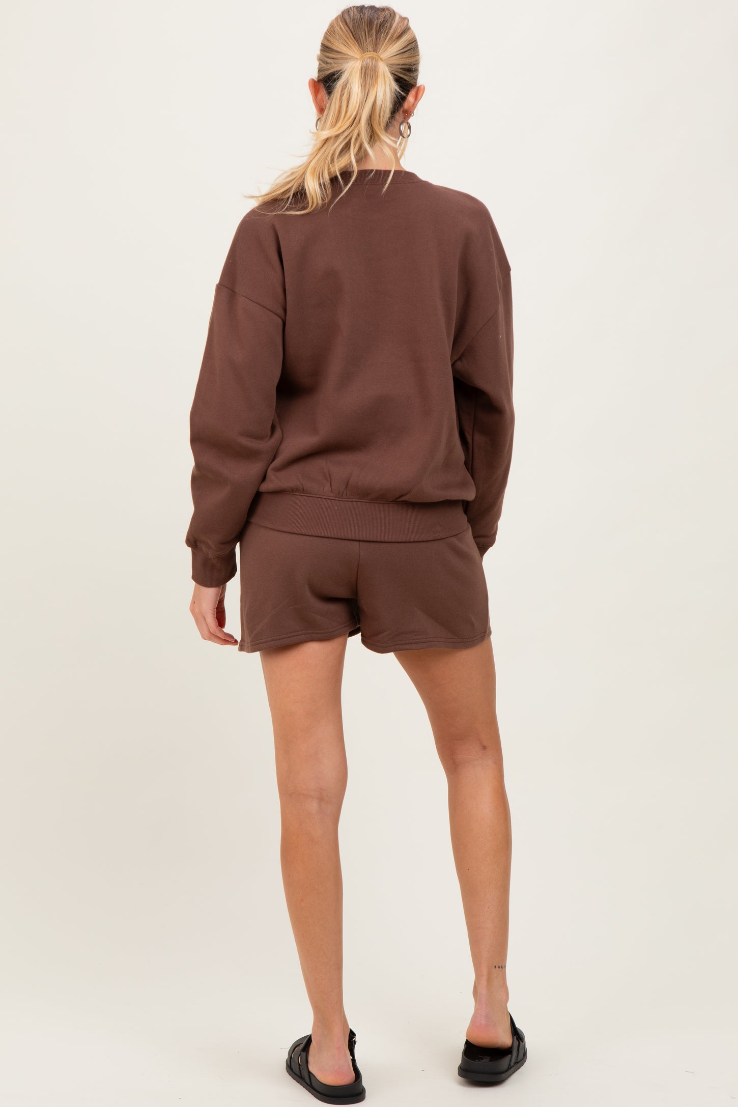 woman wearing a brown maternity sweatshirt and matching shorts, showing a relaxed fit from the back