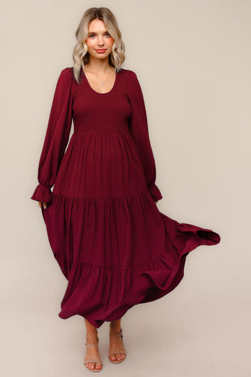 woman wearing a burgundy long sleeve smocked maxi dress with tiered ruffles and a flowy skirt