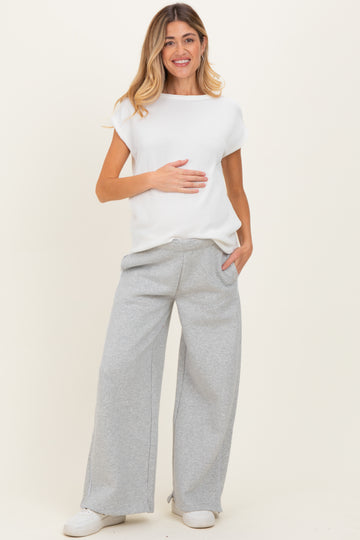 woman wearing a white ribbed maternity top and gray wide-leg sweatpants, holding her baby bump
