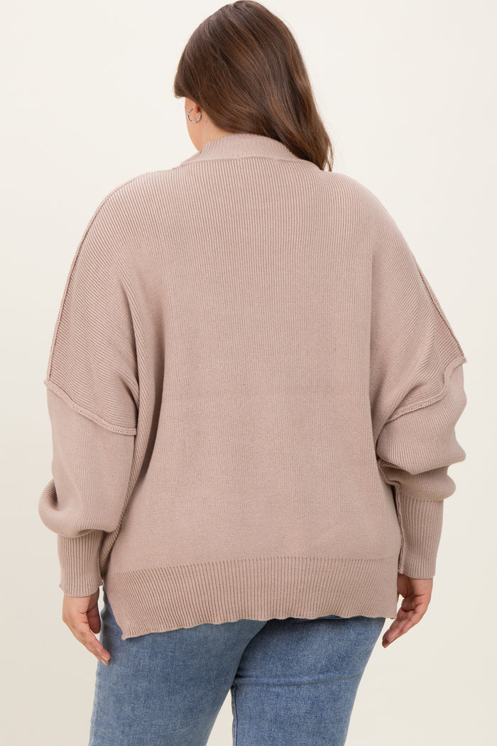 woman wearing a loose-fitting taupe maternity sweater with oversized sleeves and a ribbed texture, seen from the back