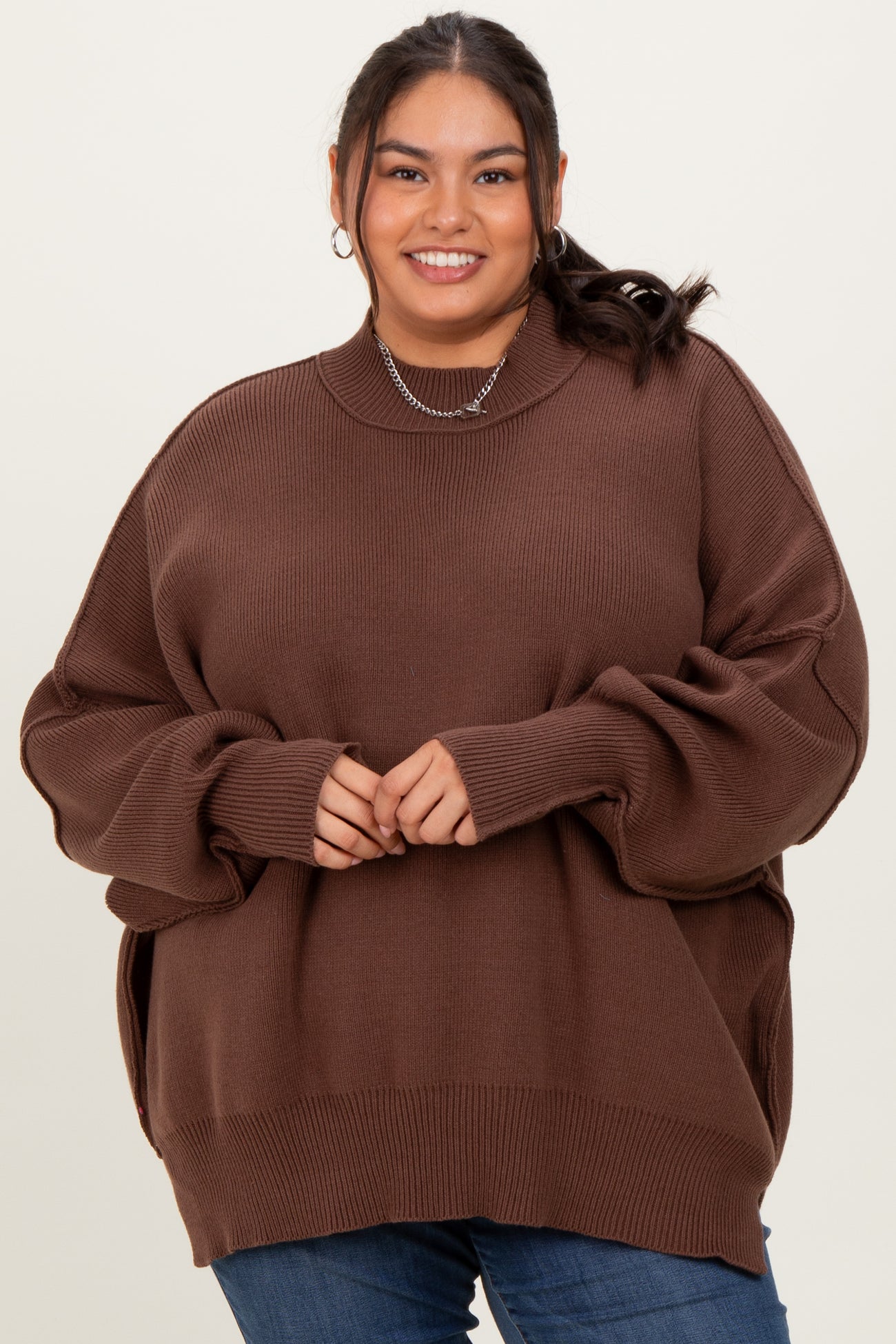 woman wearing a brown oversized ribbed sweater with a high neckline and side slits, styled with blue jeans