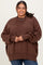 woman wearing a brown oversized ribbed sweater with a high neckline and side slits, styled with blue jeans