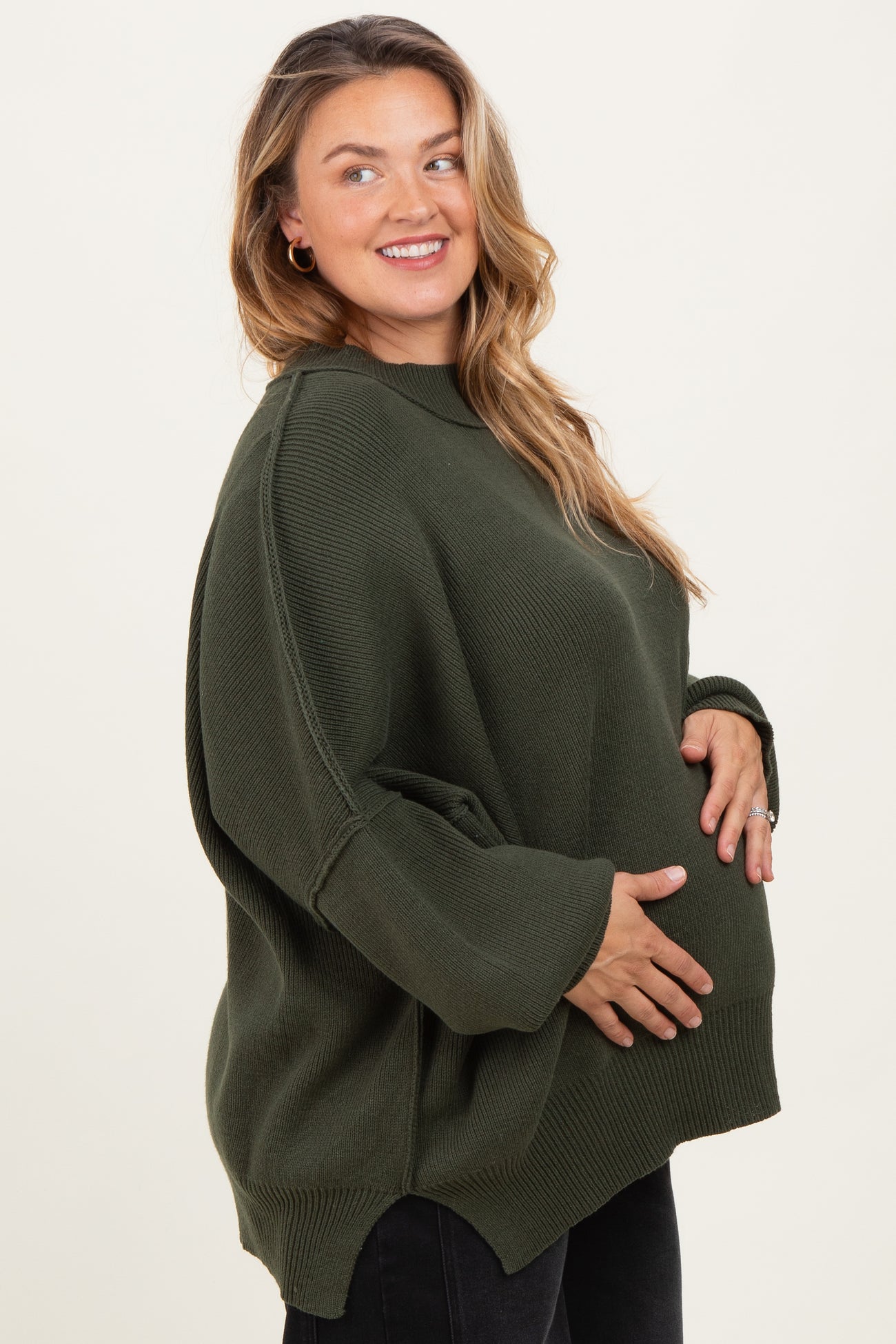 woman wearing a dark green oversized maternity sweater and holding her baby bump