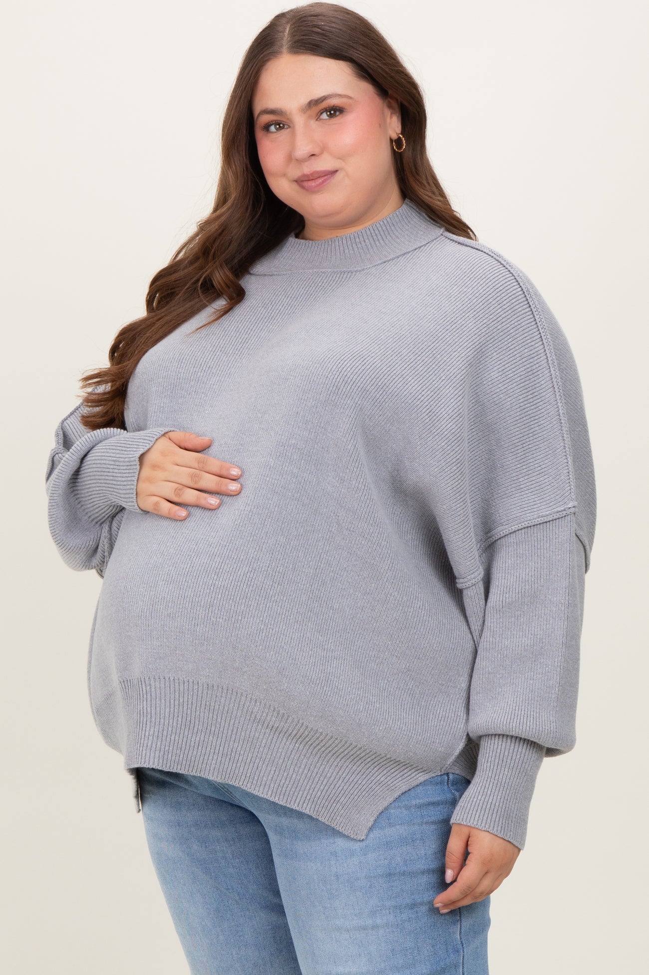 woman wearing a light gray oversized maternity sweater with a high neck and a visible baby bump