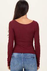 woman wearing a burgundy long sleeve top, viewed from the back, paired with light blue jeans