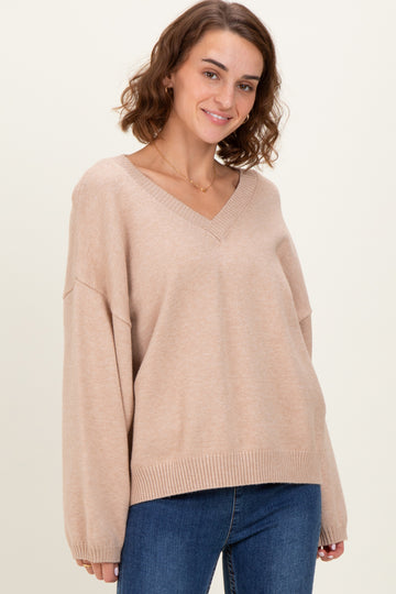 woman wearing a beige v-neck oversized sweater with long sleeves and a relaxed fit, paired with blue jeans