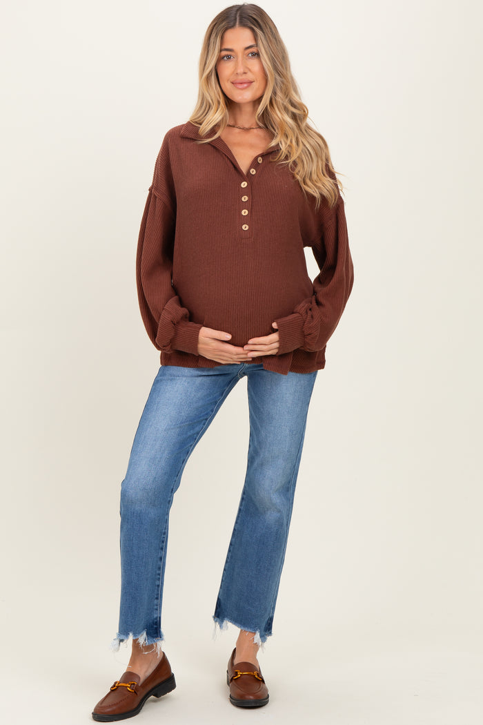 woman wearing a brown maternity pullover with button details and a baby bump, paired with light blue jeans
