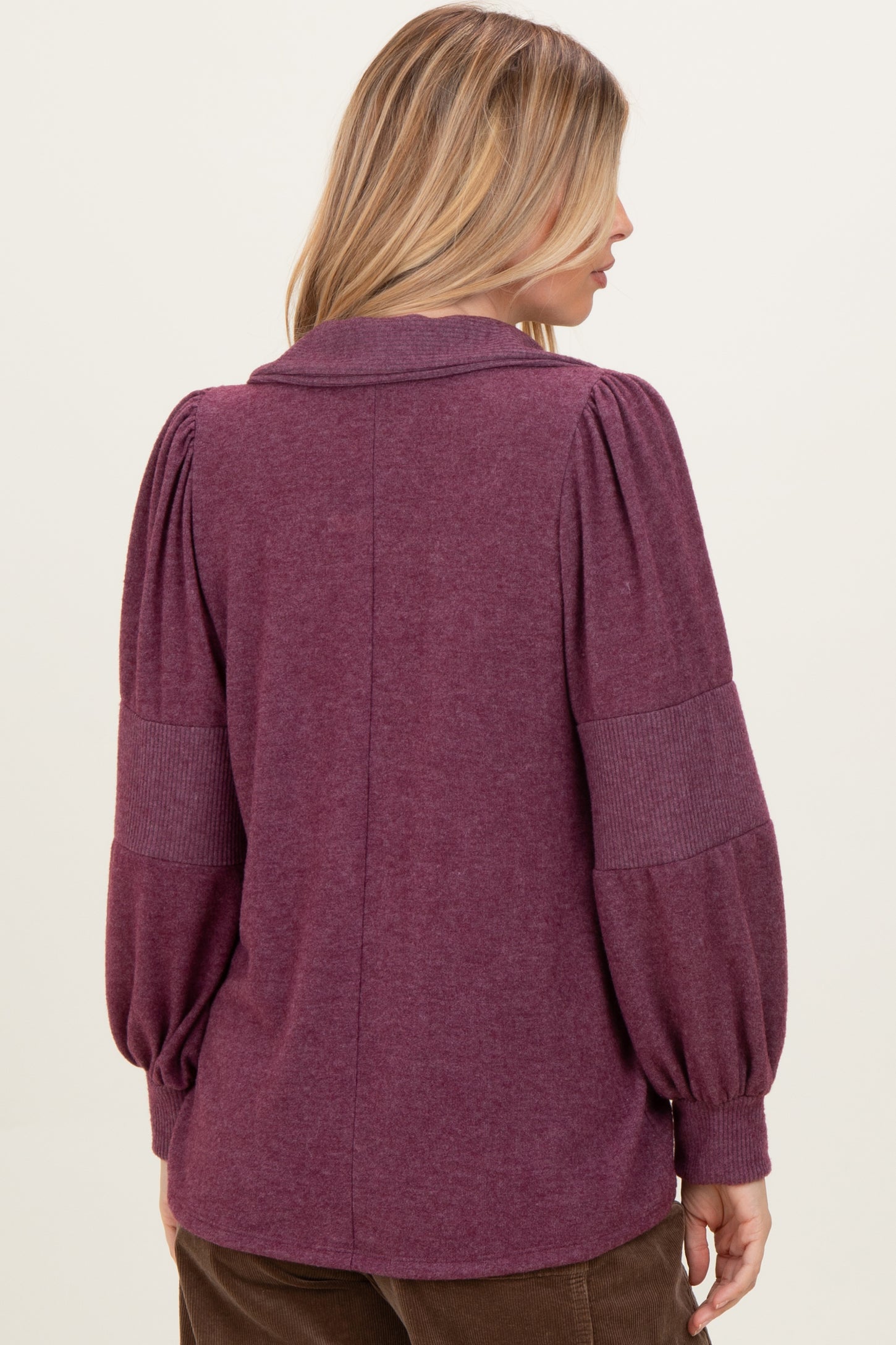 woman wearing a purple long sleeve sweater with puffed sleeves and a collar, viewed from the back