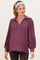 woman wearing a dark purple maternity pullover with balloon sleeves and a collared neckline, showing her baby bump