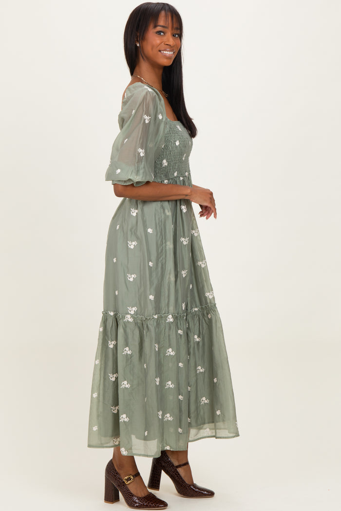 woman wearing a green floral embroidered maxi dress with puff sleeves and a tiered skirt
