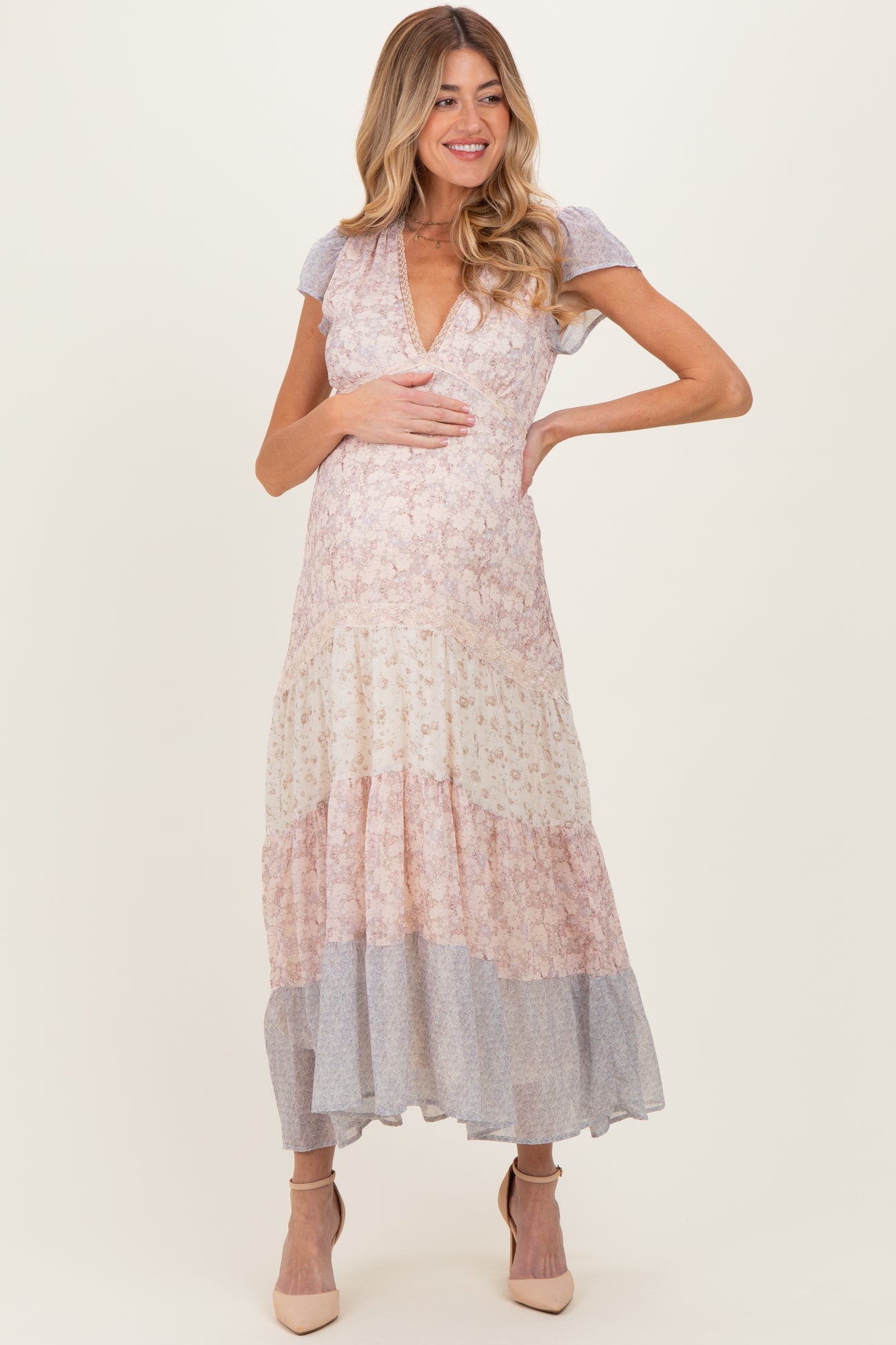 woman wearing a floral print maternity maxi dress with a deep V-neck and tiered skirt, holding her baby bump