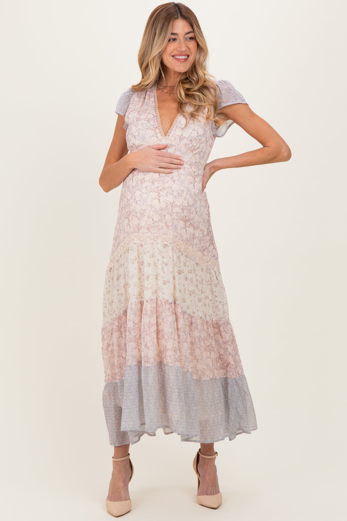woman wearing a floral print maternity maxi dress with a deep V-neck and tiered skirt, holding her baby bump