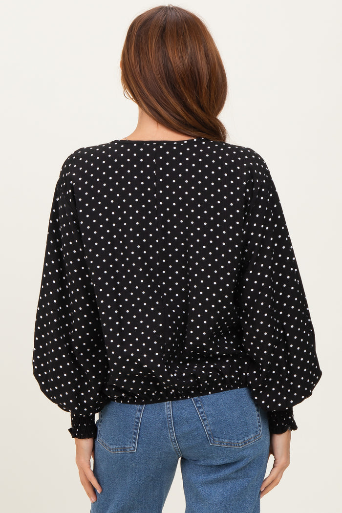 woman wearing a black polka dot blouse with puffed sleeves and a cinched waist, seen from the back