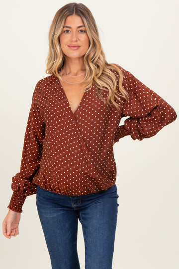 woman wearing a rust-colored maternity wrap top with white polka dots and puffed sleeves, styled with blue jeans